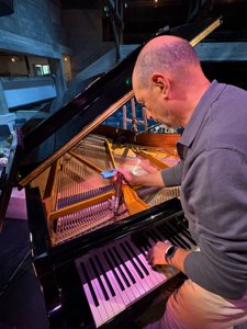 Bruno Canac à l’accord d’un piano à queue dans une salle